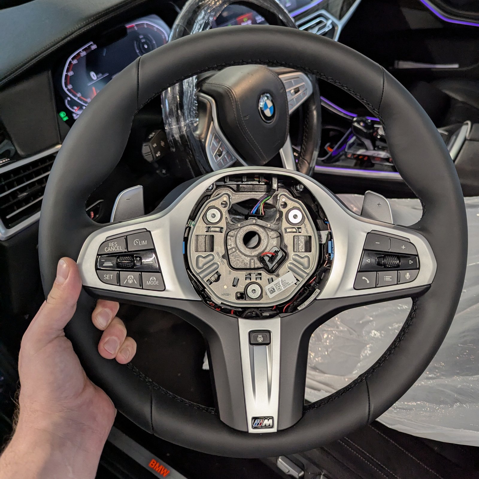 BMW M steering wheel held in front of the vehicle interior during an OEM retrofit.