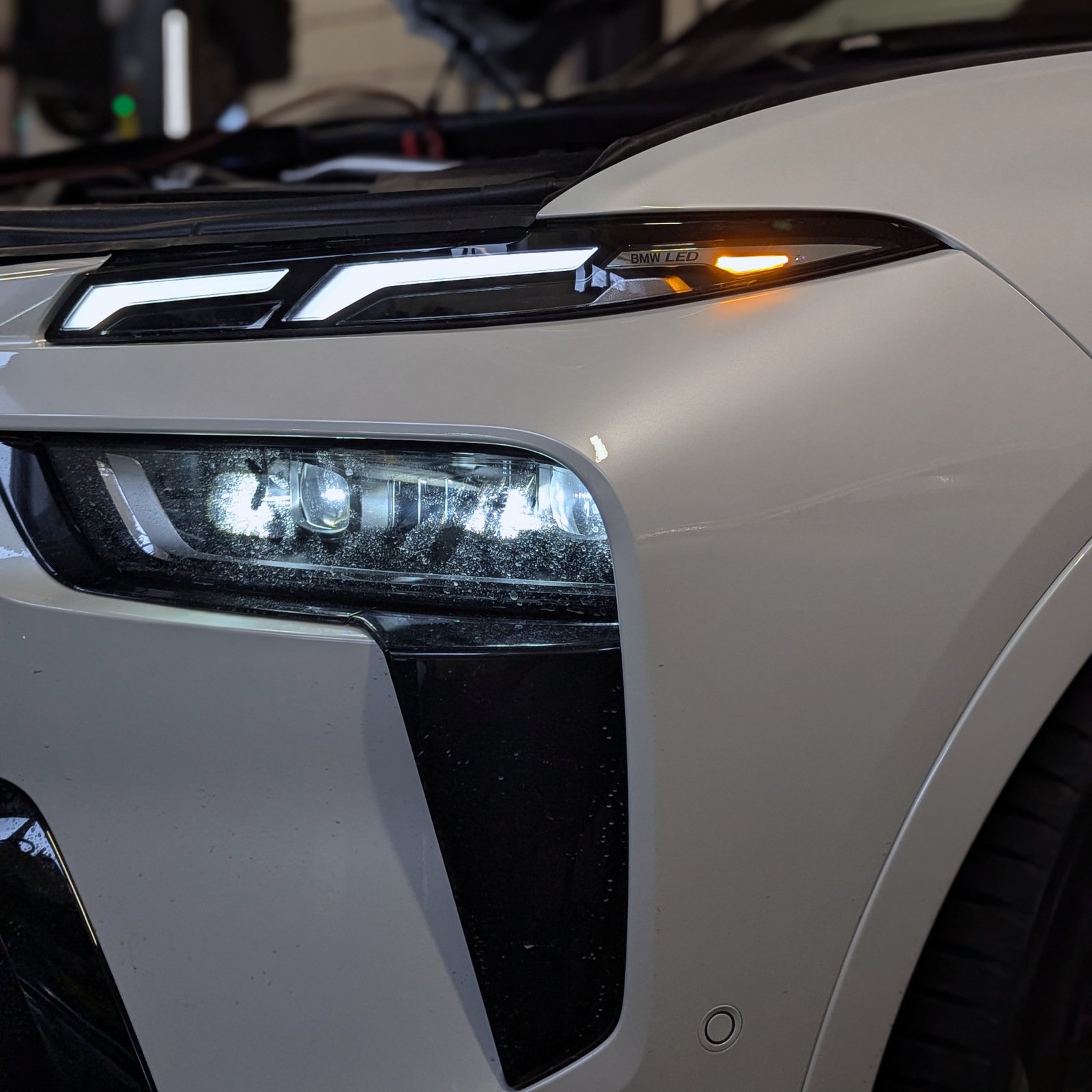 Close-up of BMW X7 front lighting with illuminated daytime running lights, headlamp and amber turn indicator.