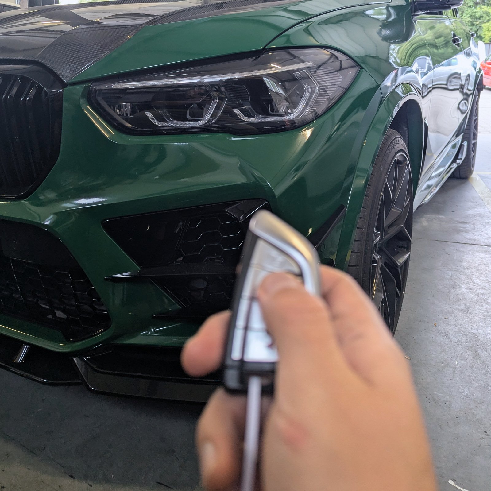 Hand holding a BMW key fob in front of a green BMW in the workshop.
