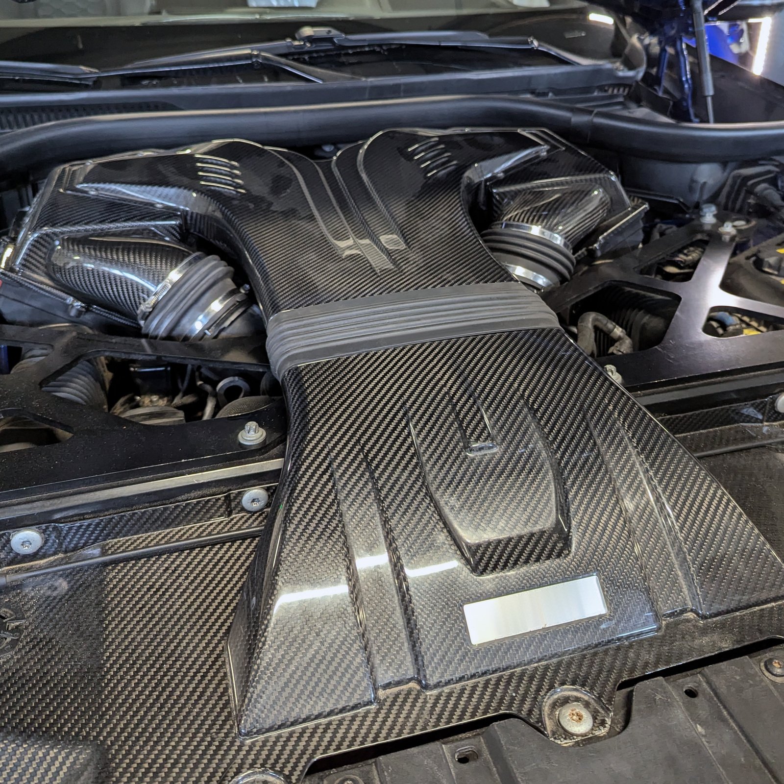 BMW engine bay with carbon-fibre intake components, hoses and structural braces.