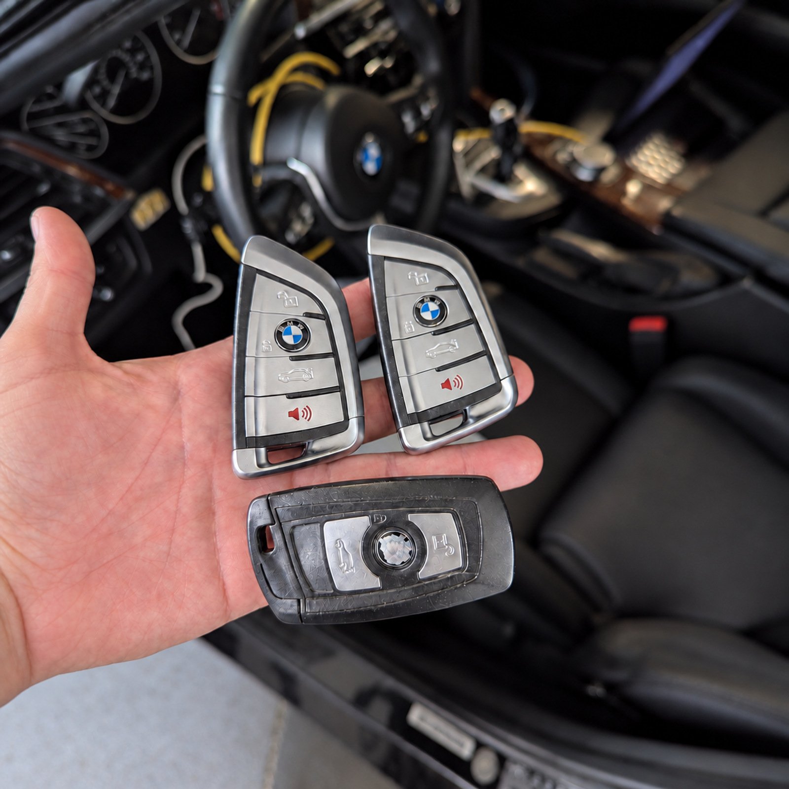 Three genuine BMW key fobs held in a hand inside a BMW vehicle.
